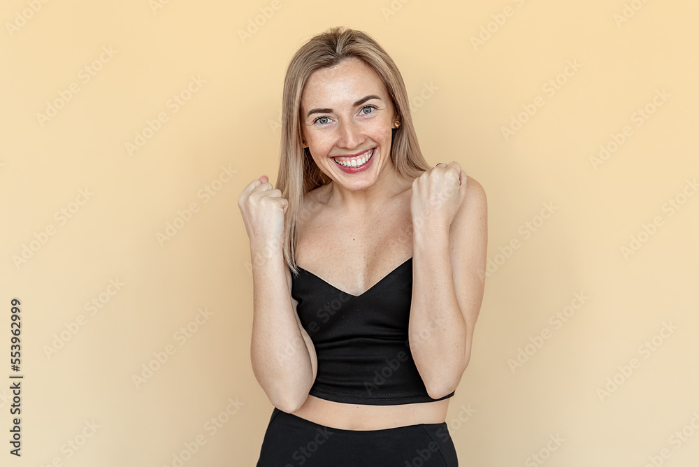 Happy stylish young woman with freckles achieve goal and celebrating, making fist pump, saying yes and smiling pleased, satisfied with smth, standing over beige background Happy stylish young woman with freckles achieve goal and celebrating, making fist pump, saying yes and smiling pleased, satisfied with smth, standing over beige background