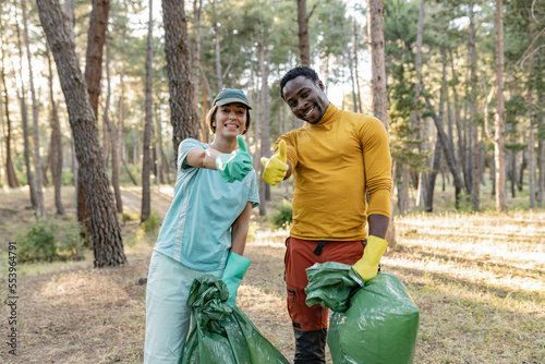 multiracial couple of volunteers cleaning the park from garbage. Walking through the forest and carrying plastic bags. Outdoor cleaning concept. © PintoArt
