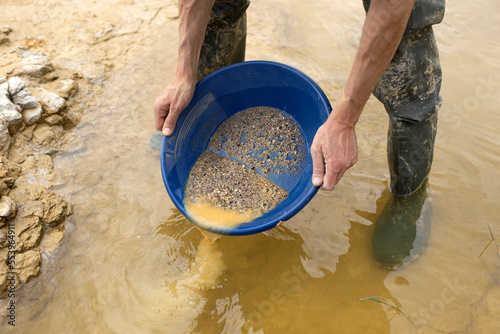 Orpailleur qui filtre la boue et le sable pour isoler des paillettes d'or à l'aide d'un tamis dans le courant d'une rivière.