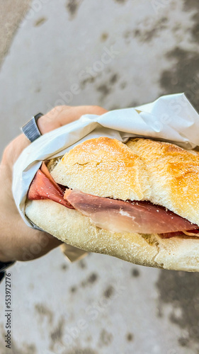 Panino appena sfornato da un panificio farcito con bresaola fresca appena affettate tenuto in mano da un cliente all'uscita di un panificio photo