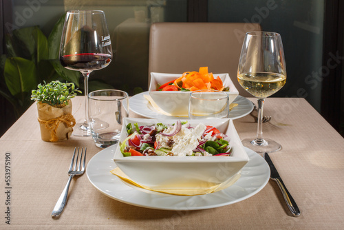 Tavolo apparecchiato di un ristorante elegante con due piatti di insalata, un calice di vino bianco ed un calice di vino rosso photo