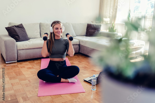 Shot of a sporty young woman using a laptop and doing lunges while dumbbells while exercising at home.