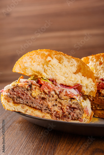 Panino da pub tagliato a metà con hamburger di carne, pomodori, insalata, bacon e cheddar servito in una braceria