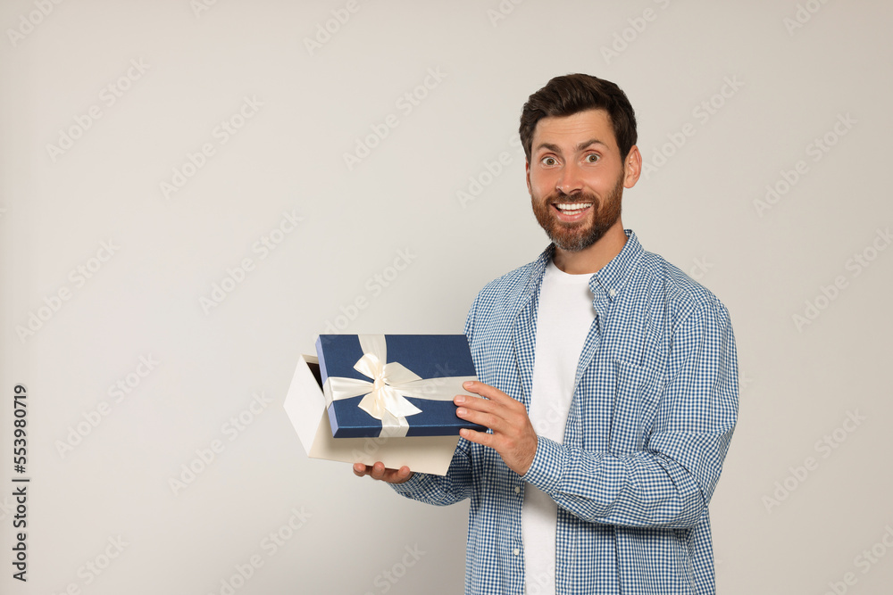 Emotional man opening gift box on light grey background, space for text Emotional man opening gift box on light grey background, space for text