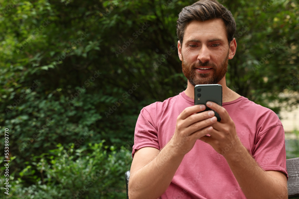 Handsome man using smartphone in park, space for text Handsome man using smartphone in park, space for text