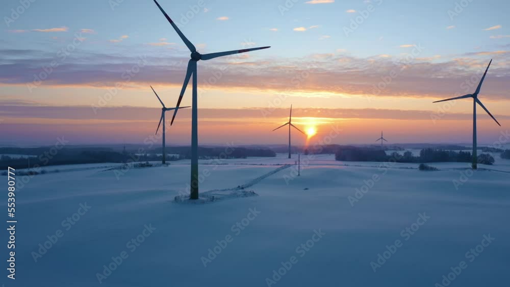 Wind turbines at sunrise in snow covered fields. Winter wind farm generating green energy