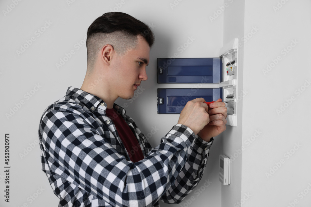 Young handyman with screwdriver repairing electrical panel board indoors