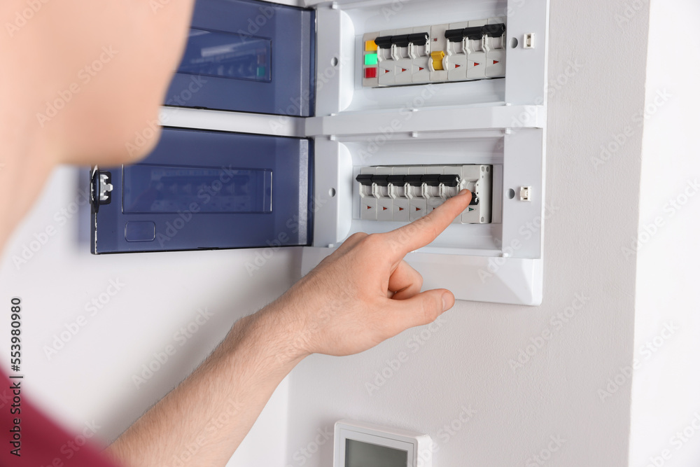 Handyman pressing switch on electrical panel board indoors, closeup Handyman pressing switch on electrical panel board indoors, closeup