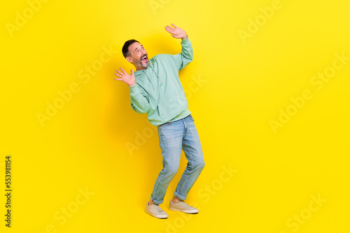 Fototapeta Naklejka Na Ścianę i Meble -  Full length photo of funky cheerful man look empty blank space ad poster raising up two arms isolated on yellow color background