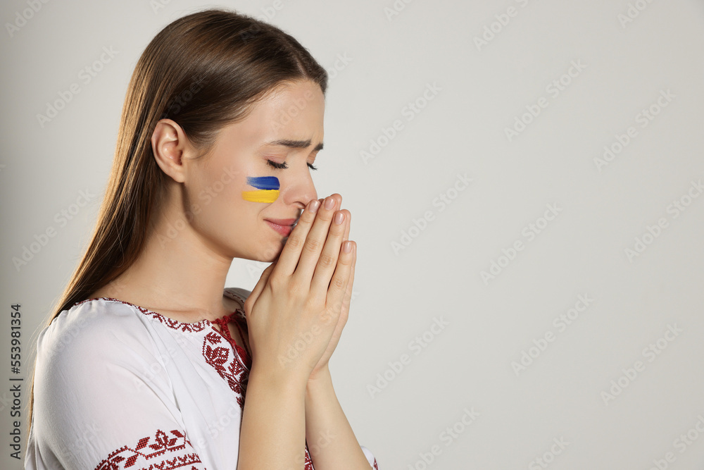 Sad young Ukrainian woman with clasped hands on beige background, space for text Sad young Ukrainian woman with clasped hands on beige background, space for text