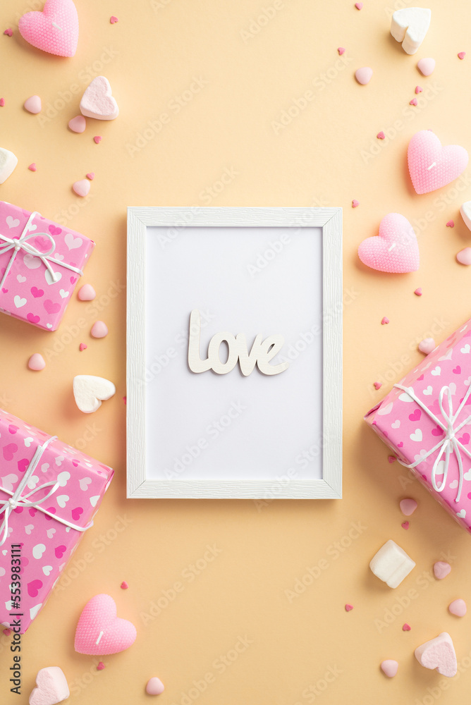 Valentine's Day concept. Top view vertical photo of photo frame with inscription love gift boxes heart shaped marshmallow candles and sprinkles on isolated beige background