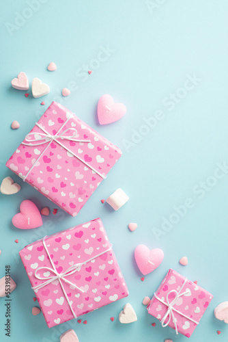 St Valentine's Day concept. Top view vertical photo of pink present boxes heart shaped marshmallow candles and sprinkles on isolated light blue background with copyspace © ActionGP