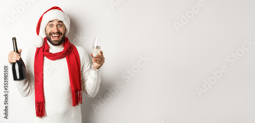 Christmas party and holidays concept. Happy bearded male model in Santa hat and red scarf, celebrating xmas, partying with glass of Champgne, white background photo