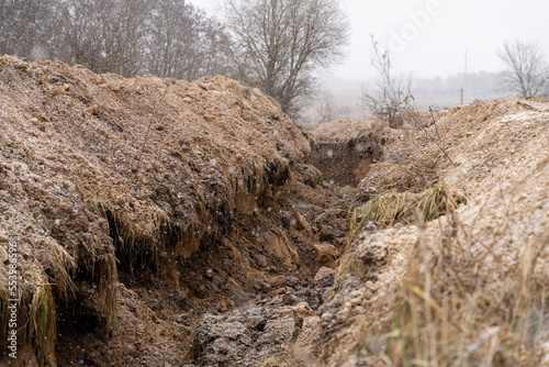 Obraz na płótnie winter landscape, anti-tank ditch near the road. engineering military constructions on the line of defense. war in Ukraine, defensive positions w salonie