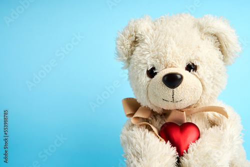 Teddy bear holding heart on blue background with copy space © Gecko Studio