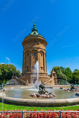 Lovely view of the famous Water Tower (Wasserturm) and the fountain with water spouts in front on a sunny day with blue sky in Mannheim, Germany. On the conical copper roof is a statue of Amphitrite.