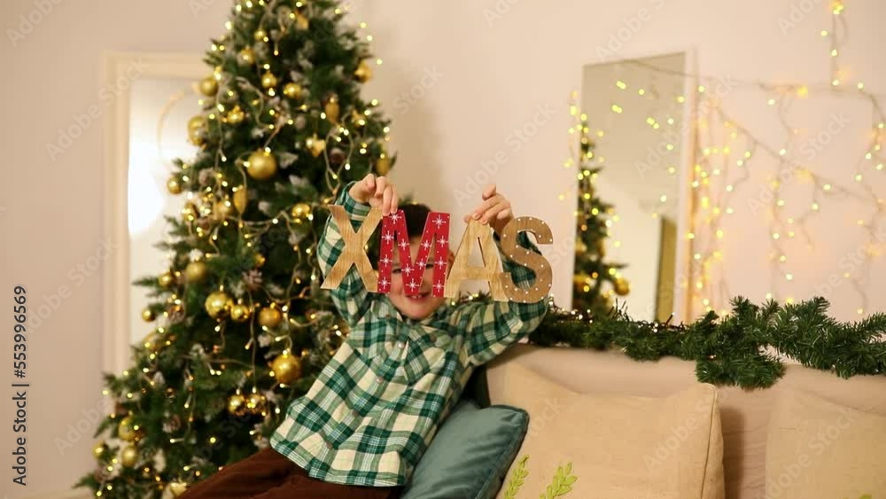 Boy shows wooden letters that say Christmas. Christmas is coming. Boy covers his face with the inscription Christmas Boy shows wooden letters that say Christmas. Christmas is coming. Boy covers his face with the inscription Christmas