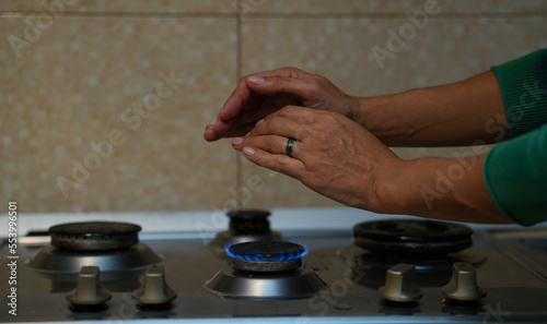 two female hands warming above the stove flame. detail.
