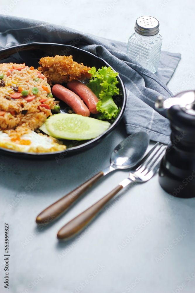 Fried rice with peanuts, carrots, raisins Served with fried chicken, fried egg, and fried sausage. Served on a black plate on a white table in a restaurant. Fried rice with peanuts, carrots, raisins Served with fried chicken, fried egg, and fried sausage. Served on a black plate on a white table in a restaurant.