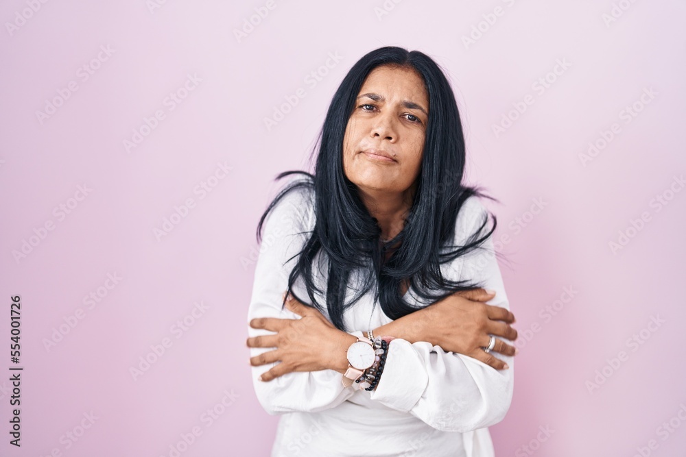 Mature hispanic woman standing over pink background shaking and freezing for winter cold with sad and shock expression on face Mature hispanic woman standing over pink background shaking and freezing for winter cold with sad and shock expression on face