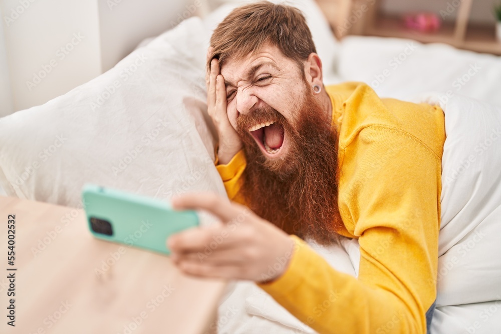 Young redhead man waking up by smartphone alarm at bedroom Young redhead man waking up by smartphone alarm at bedroom