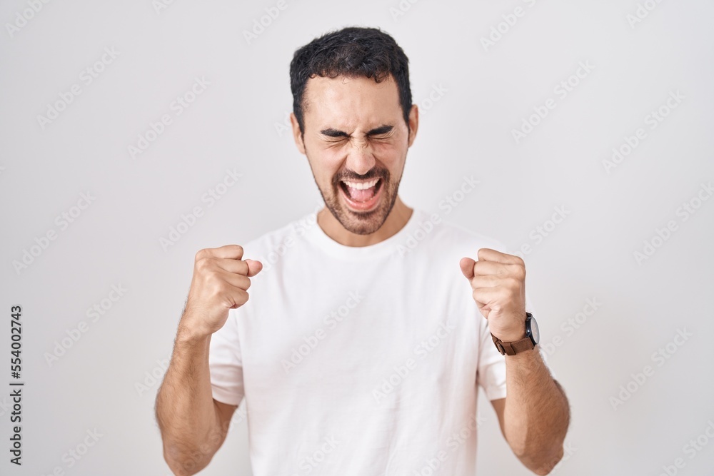 Handsome hispanic man standing over white background excited for success with arms raised and eyes closed celebrating victory smiling. winner concept. Handsome hispanic man standing over white background excited for success with arms raised and eyes closed celebrating victory smiling. winner concept.
