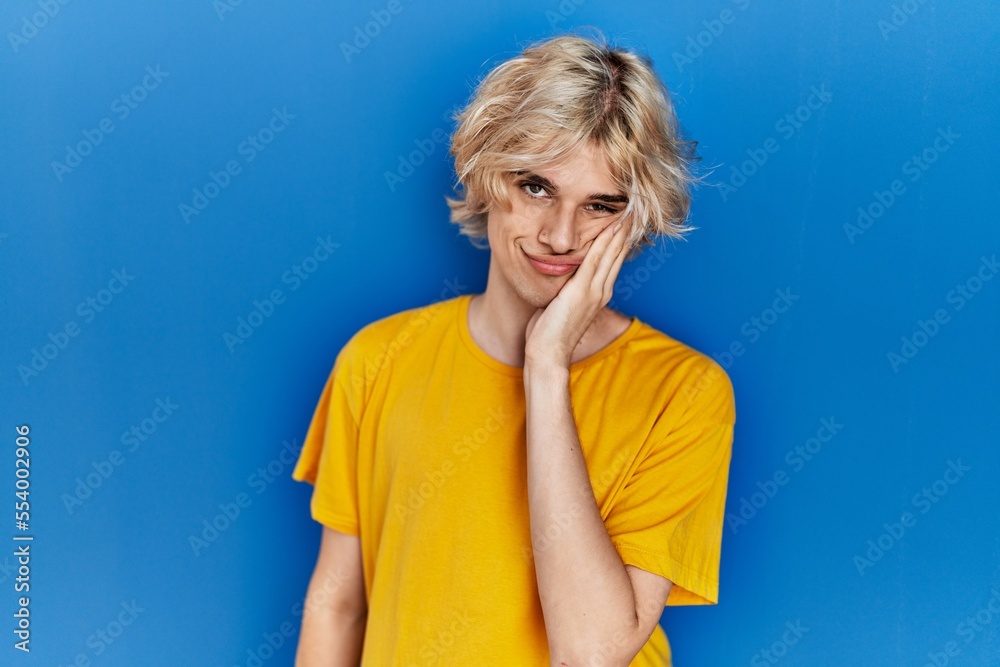Young modern man standing over blue background thinking looking tired and bored with depression problems with crossed arms. Young modern man standing over blue background thinking looking tired and bored with depression problems with crossed arms.