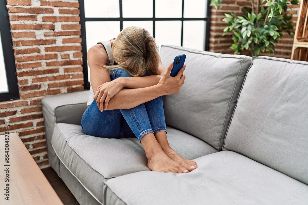 Fototapeta premium Young blonde woman depressed using smartphone at home