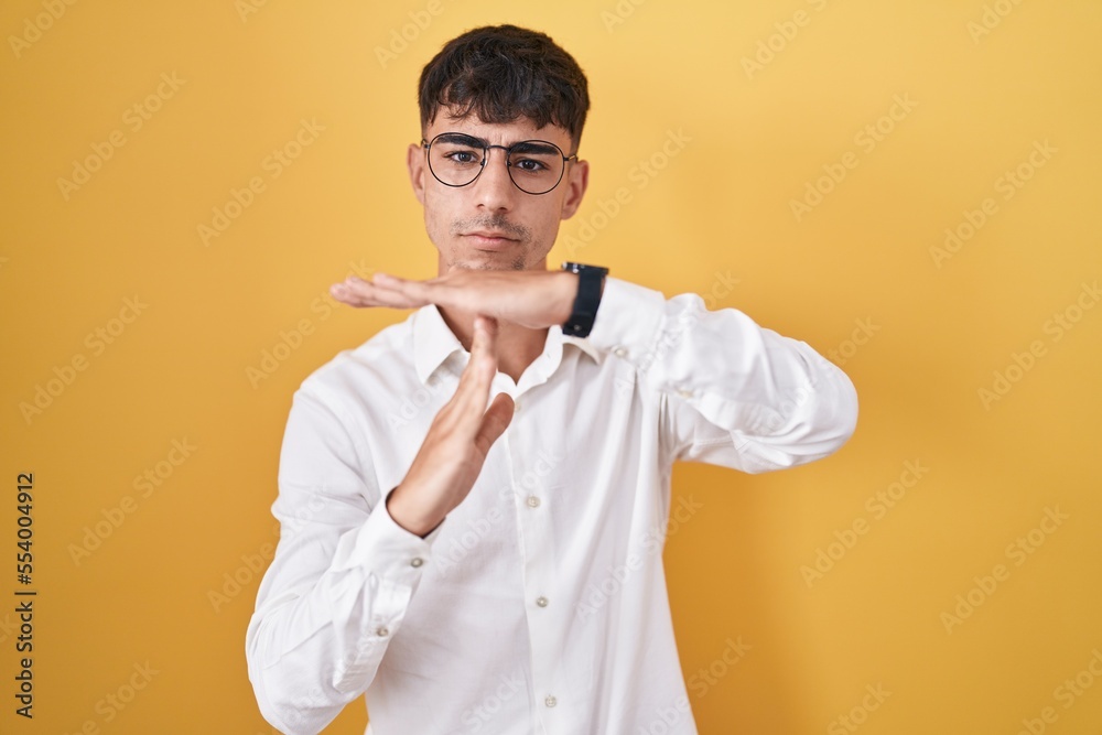 Young hispanic man standing over yellow background doing time out gesture with hands, frustrated and serious face Young hispanic man standing over yellow background doing time out gesture with hands, frustrated and serious face