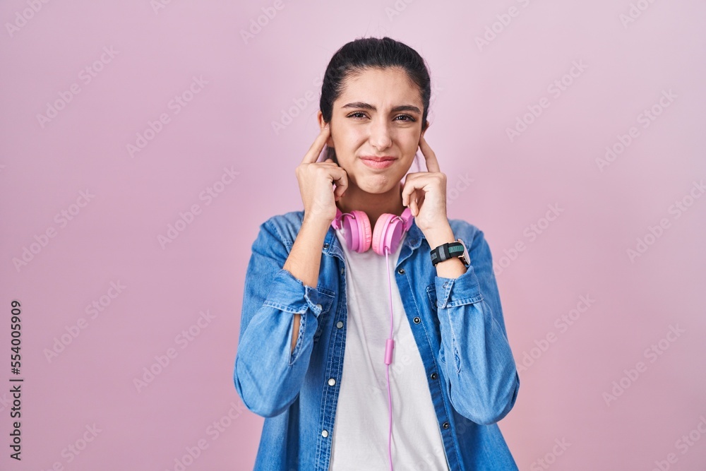 Young beautiful woman standing over pink background covering ears with fingers with annoyed expression for the noise of loud music. deaf concept. Young beautiful woman standing over pink background covering ears with fingers with annoyed expression for the noise of loud music. deaf concept.