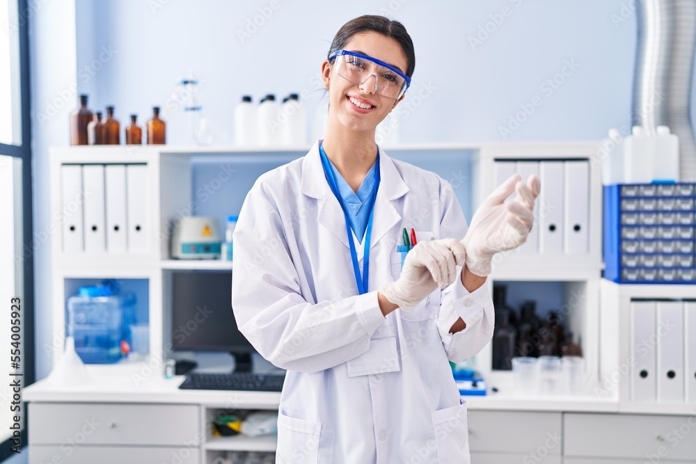 Young beautiful hispanic woman scientist smiling confident wearing gloves at laboratory