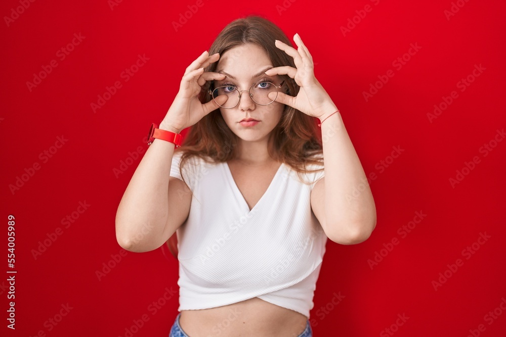 Young caucasian woman standing over red background trying to open eyes with fingers, sleepy and tired for morning fatigue