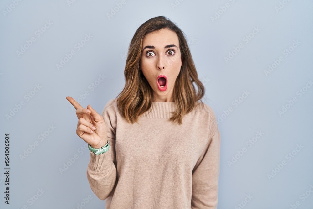 Young woman standing over isolated background surprised pointing with finger to the side, open mouth amazed expression. Young woman standing over isolated background surprised pointing with finger to the side, open mouth amazed expression.