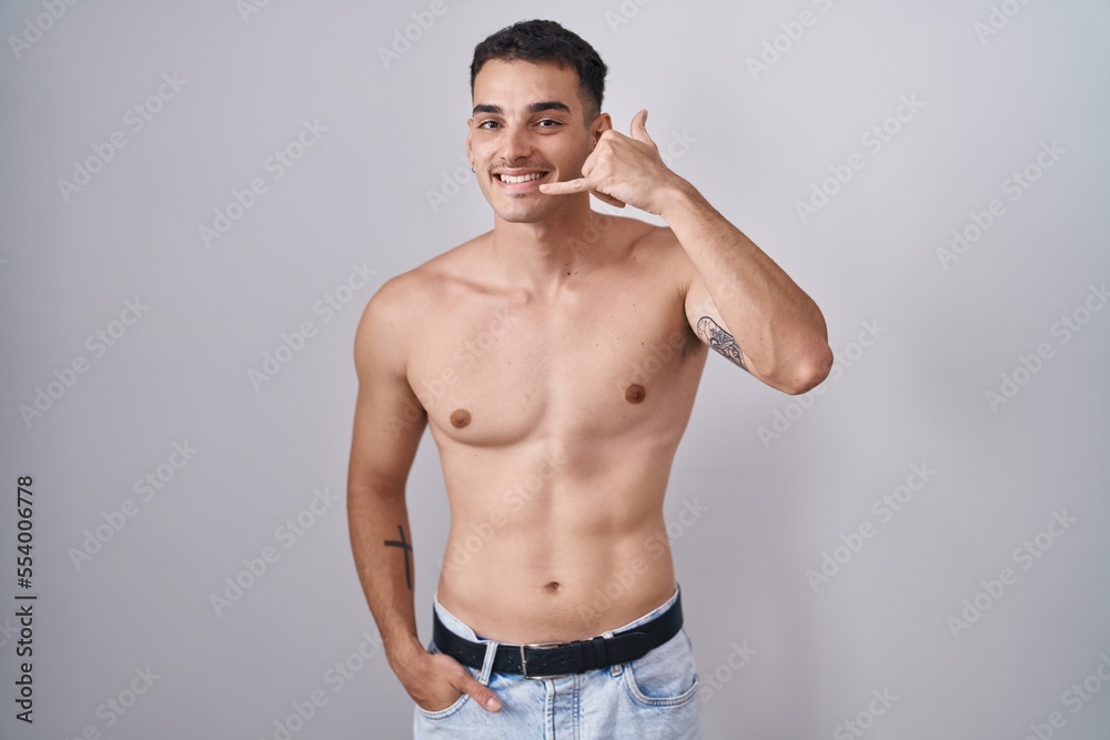 Fototapeta premium Handsome hispanic man standing shirtless smiling doing phone gesture with hand and fingers like talking on the telephone. communicating concepts.