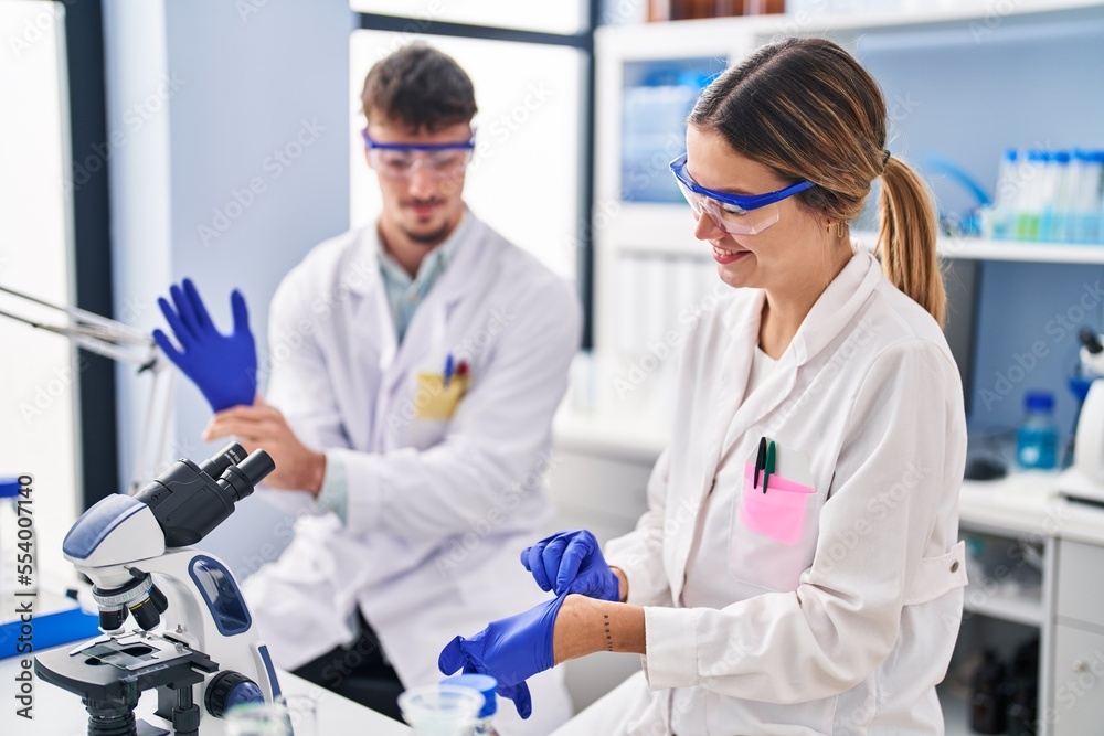 Young man and woman scientists workers wearing gloves at laboratory Young man and woman scientists workers wearing gloves at laboratory