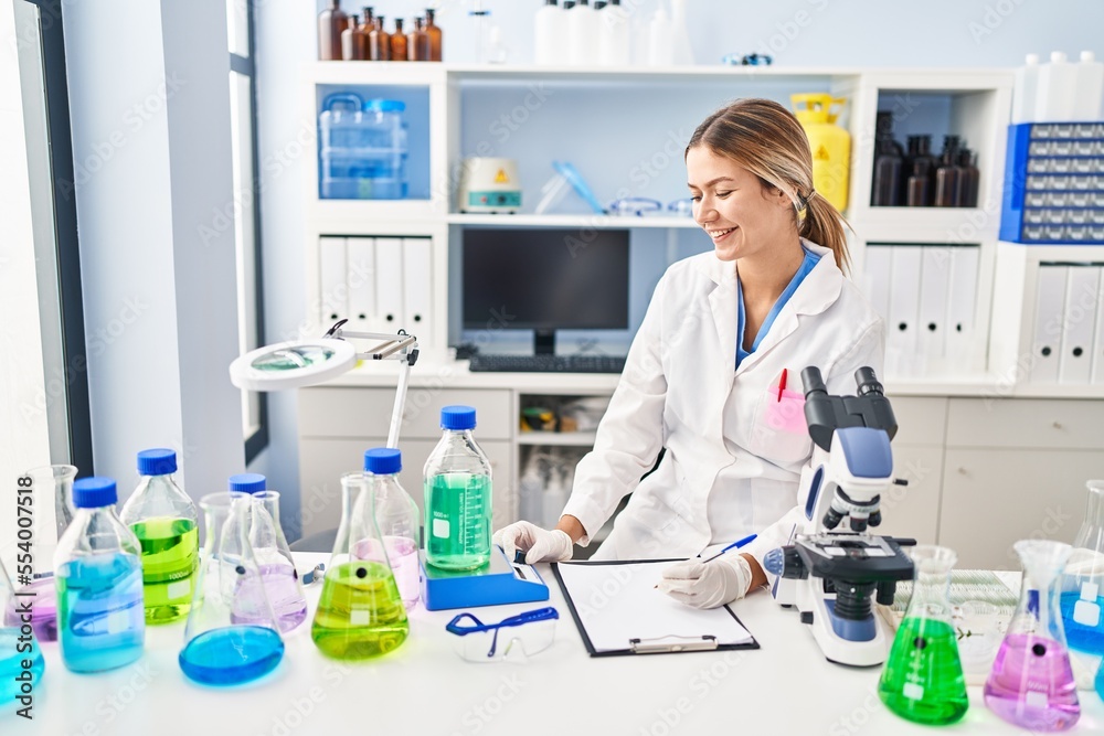 Young hispanic woman scientist measuring liquid write on document at laboratory Young hispanic woman scientist measuring liquid write on document at laboratory