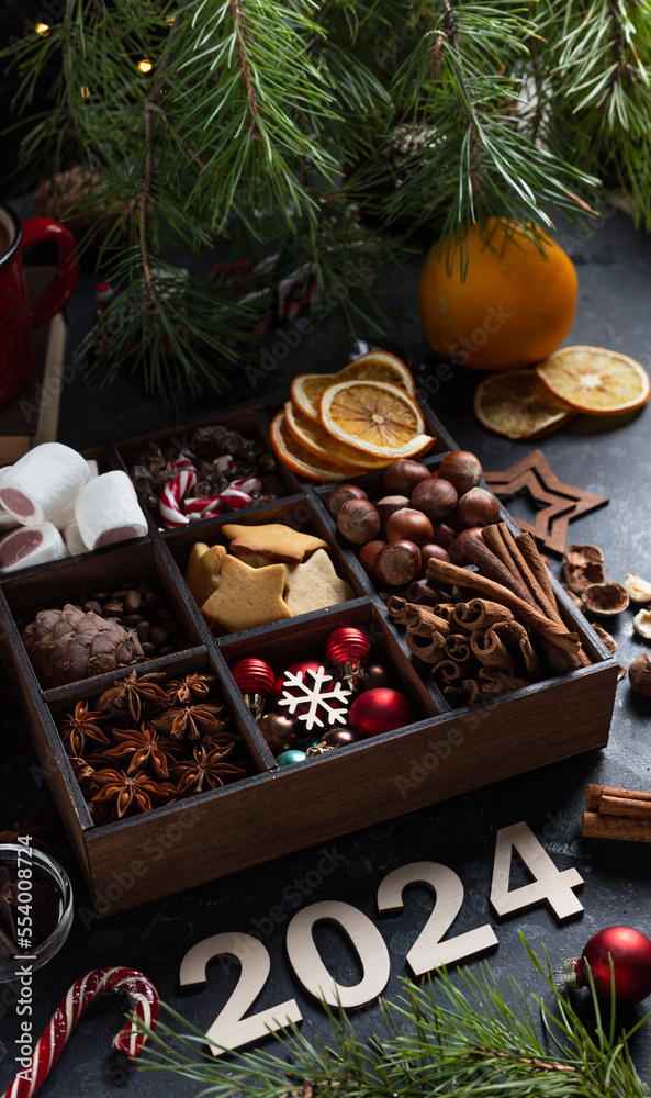 On the table there is a box with nine compartments in which nuts, cookies and spices are poured. On top are the numbers 2024 On the table there is a box with nine compartments in which nuts, cookies and spices are poured. On top are the numbers 2024