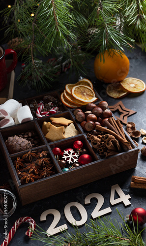 On the table there is a box with nine compartments in which nuts, cookies and spices are poured. On top are the numbers 2024