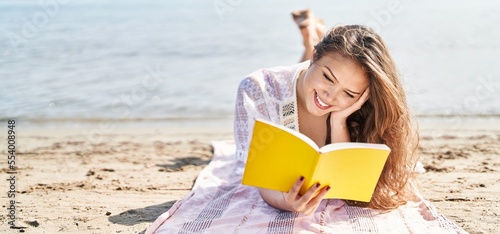 Foto Young beautiful hispanic woman tourist reading book lying on sand at beach