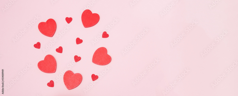 Red wooden hearts on a pink background. The concept of Valentine's day, love, dating and wedding. Symbol of a romantic gift or marriage proposal. Copy space, web banner.