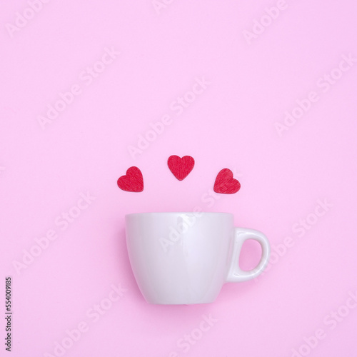 Coffee cup and red wooden hearts on a pink background. The concept of Valentine's day, love, dating and wedding. Symbol of a romantic gift or marriage proposal. Copy space, minimalism, square photo.