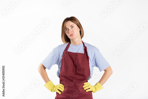 Sad and tired woman wearing apron and rubber gloves standing isolated on white background