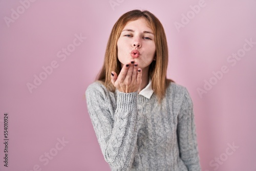 Beautiful woman standing over pink background looking at the camera blowing a kiss with hand on air being lovely and sexy. love expression.