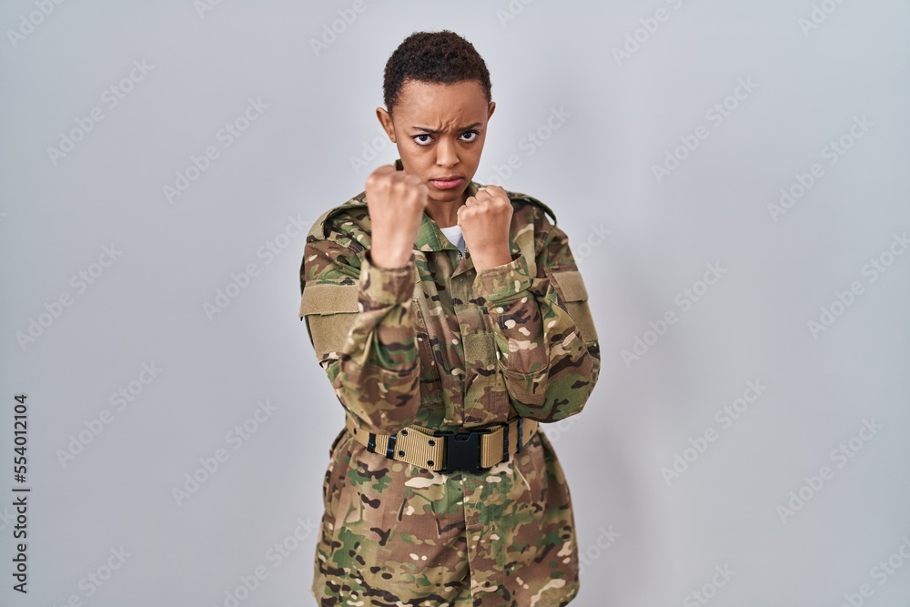 Beautiful african american woman wearing camouflage army uniform ready to fight with fist defense gesture, angry and upset face, afraid of problem