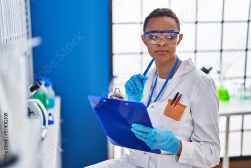 African american woman scientist writing on document with doubt expression at laboratory