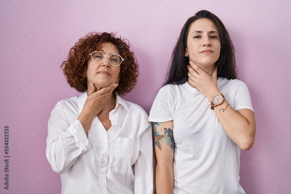 Hispanic mother and daughter wearing casual white t shirt over pink background touching painful neck, sore throat for flu, clod and infection Hispanic mother and daughter wearing casual white t shirt over pink background touching painful neck, sore throat for flu, clod and infection