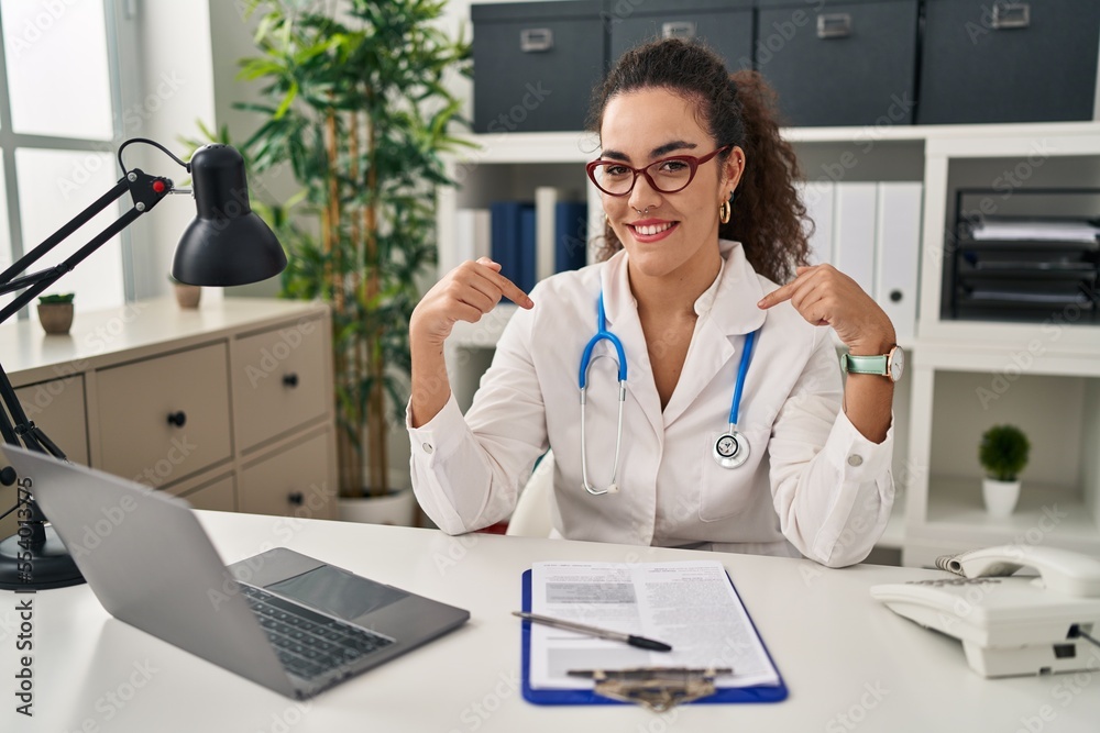 Young hispanic woman wearing doctor uniform and stethoscope looking confident with smile on face, pointing oneself with fingers proud and happy. Young hispanic woman wearing doctor uniform and stethoscope looking confident with smile on face, pointing oneself with fingers proud and happy.