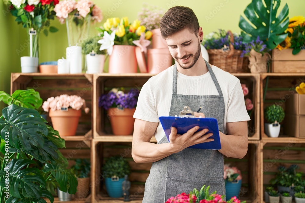 Young caucasian man florist smiling confident writing on document at flower shop