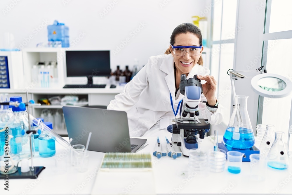 Young hispanic woman wearing scientist uniform using laptop and microscope at laboratory Young hispanic woman wearing scientist uniform using laptop and microscope at laboratory