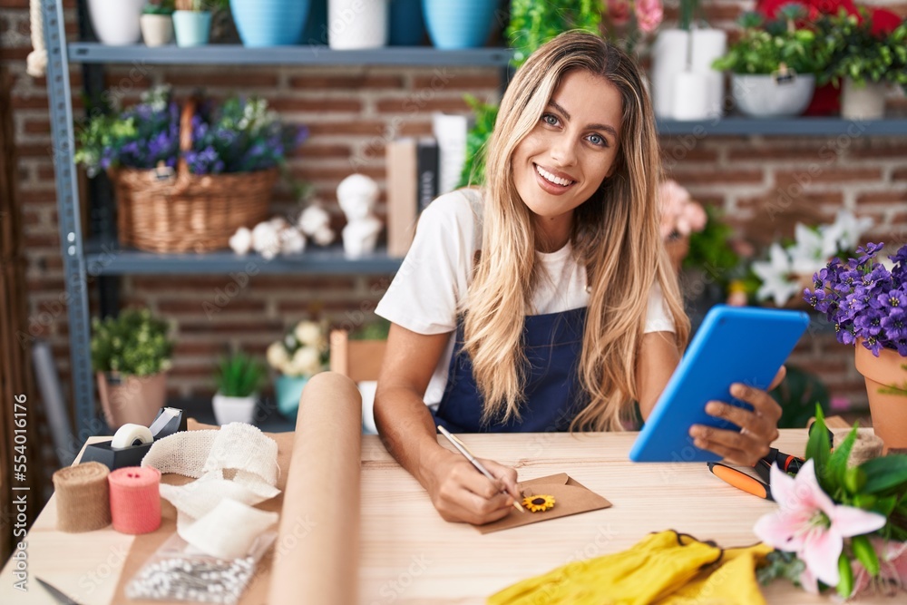 Young blonde woman florist using touchpad writing on envelope letter at florist Young blonde woman florist using touchpad writing on envelope letter at florist
